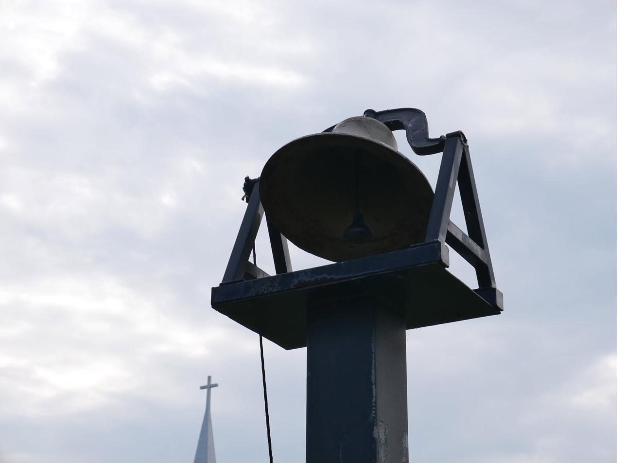 Church bell against the sky with the sanctuary steeple in the distance